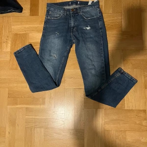 Blå jeans med slitningar - Snygga blå jeans med slitningar på framsidan för en trendig look. De har en klassisk femficksdesign och en bekväm passform. Perfekta för en avslappnad stil. Priset kan diskuteras