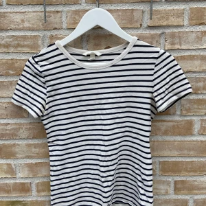 Randig t-shirt från H&M🌟 - KRYMT - NU STRL XS! Säljer en klassisk randig t-shirt från H&M i svart och vit. T-shirten har korta ärmar och en rund halsringning, perfekt för en avslappnad stil. Mycket skön! 