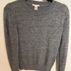 Grå stickad tröja - Mysig grå stickad tröja med rund hals och långa ärmar. Perfekt för kyliga dagar och enkel att matcha med olika outfits.