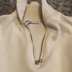 Beige tröja med dragkedja från Zara - Säljer en stilren beige tröja från Zara med halv dragkedja och hög krage. Tröjan har långa ärmar och ribbade muddar vid ärmslut och nederkant. Perfekt för en avslappnad look.