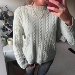 Ljusgrön stickad tröja - Säljer en mysig ljusgrön stickad tröja med kabelstickat mönster. Tröjan har långa ärmar och en rund halsringning, perfekt för kyligare dagar. Passar bra till jeans eller kjol för en avslappnad look. I 100% kashmir