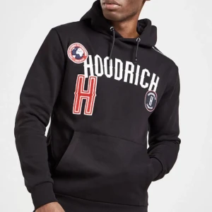 Svart hoodie från Hoodrich - Snygg svart hoodie från Hoodrich med tryck i vitt och rött på framsidan. Den har en stor ficka framtill och en huva. Använd några gånger men är i bra skick. Snöret till huvan saknas. Nypris 800