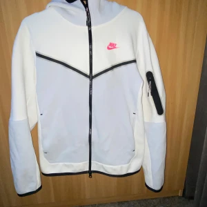 Vit hoodie från Nike - Säljer en stilren vit hoodie från Nike med svart dragkedja och rosa logga på bröstet. Hoodien har en praktisk ficka på ärmen och svarta detaljer vid ärmslut och nederkant. Hoodie och det endast använda 1-2 veckor allt är perfekt skick (ingen skador & fläck) skriv för mer bilder eller vid intresse. Pris kan diskuteras 😃