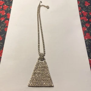 Glittrigt halsband med triangulärt hänge - Snyggt vintage halsband från USA med ett stort triangulärt hänge täckt av glittrande stenar. Kedjan är också dekorerad med små stenar som ger extra bling. Perfekt för att lysa upp vilken outfit som helst.