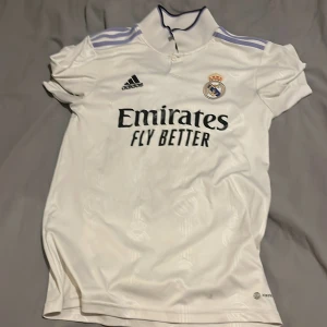 Real Madrid 2022/2023 - Säljer en vit Real Madrid fotbollströja från Adidas med korta ärmar och klubbens emblem på bröstet.  Perfekt för alla fotbollsfans 