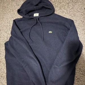 Mörkblå hoodie från Lacoste - Snygg mörkblå wool hoodie från Lacoste med det klassiska krokodilmärket på bröstet. Skick 8/10 använd fåtal gånger 