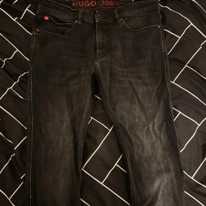 Svarta jeans från Hugo - Snygga svarta jeans från Hugo med klassisk femficksdesign och röd logotypdetalj på baksidan. Perfekta för en stilren look, den är använd maximalt 2 gånger. Inga fläckar och inga skador på byxorna. Pris kan diskuteras och byten kan möjligtvis gå igenom.