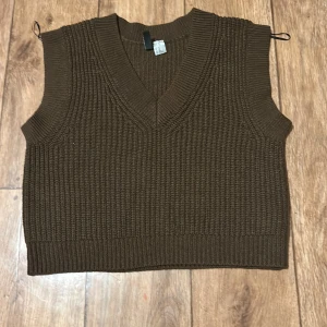 Brun stickad väst från H&M - Säljer en snygg brun stickad väst från H&M. Västen har en v-ringad design och är perfekt för lager-på-lager-stil. Den ribbade strukturen ger en modern touch.