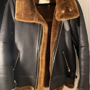 Svart skinnjacka med brun päls från Zara - Säljer en snygg svart skinnjacka från Zara med mjuk brun pälsfoder. Jackan har dragkedja och två fickor med dragkedjor. 