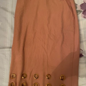 Rosa kjol med ringdetaljer - Säljer en superfin rosa kjol med coola ringdetaljer längst ner. Kjolen är i ett ribbat material som ger en snygg struktur och passar perfekt för både vardag och fest. Den har en tight passform som framhäver figuren. Perfekt för vår och sommar!