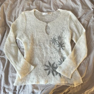 Vit stickad tröja med blommönster - Säljer en superfin vit stickad tröja med ett grått blommönster på framsidan. Den har en unik nyckelhålsdetalj vid halsen och långa ärmar. Perfekt för både vår och höst! 🧶