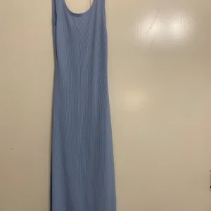 Ljusblå ribbad långklänning - Säljer en ljusblå långklänning i ribbat material. Den har en snygg slits på sidan och en öppen ryggdetalj.