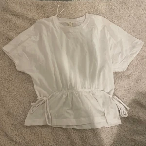 Vit kortärmad topp med knyten - Säljer en superfin vit topp med korta ärmar och knytband i midjan. Bra skick, kommer inte till användning. Köpt från hm! Storlek XS men sitter som en S