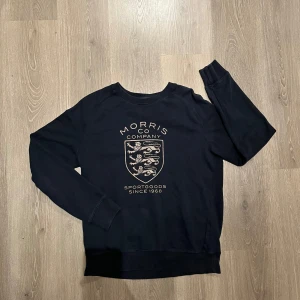Mörkblå sweatshirt från Morris - Säljer en mörkblå sweatshirt från Morris med ett coolt tryck på framsidan. Tröjan är i mycket bra skick och har långa ärmar. Perfekt för en avslappnad stil eller för att hålla sig varm under kyligare dagar. Passar både till vardags och för lite sportigare tillfällen.