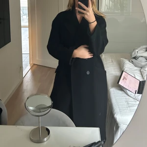 Svart kappa från Zara - Säljer en svart kappa från Zara i storlek S. Den har en klassisk design med knappar framtill och är perfekt för höst och vinter. Kappan är i bra skick och men med tecken på användning. 