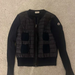 Marinblå Moncler Cardigan - Säljer en snygg marinblå Moncler jacka. Den har en quiltad design med dragkedja framtill och långa ärmar. Jackan är i storlek XS🤍