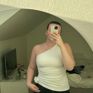 Vit oneshoulder topp - Säljer en snygg vit oneshoulder topp med blomdetaljer🥰