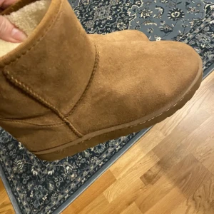 Bruna uggs  - Säljer ett par bruna boots i mocka med mjukt foder inuti. Perfekta för kalla dagar med sin varma och bekväma design. De har en enkel och stilren look utan snörning eller dragkedja.