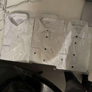 Vit skjorta från Eton - Säljer tre stilrena vita skjortor från Eton i nytt skick. Perfekta för både formella och avslappnade tillfällen. Skjortorna har en klassisk design med knappar och är tillverkade i högkvalitativt material för en bekväm passform. Passar utmärkt till både kostym och jeans. Säljer 1 för 400kr och alla för 1000kr. OANDVÄNDA