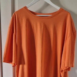Orange t-shirt i polyester - Säljer en enkel och bekväm orange t-shirt i 100% polyester. Perfekt för vardagsbruk med en lös passform och korta ärmar. Tillverkad i Kina. Passar bra till både sommar och vår.