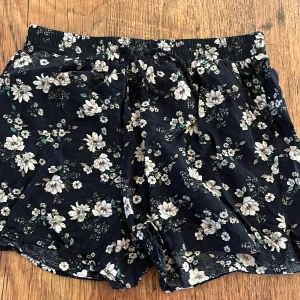 Blommiga shorts  - Blommiga shorts med blå bakgrund i storlek 146/152  men passar en xs. 