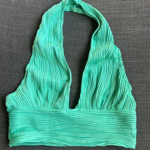 Grön ribbad halterneck topp - Snygg grön halterneck topp med ribbad textur. Perfekt för sommardagar eller en festkväll. Toppen har en tight passform och är tillverkad i ett mjukt, stretchigt material. Den är ärmlös och har en stilren design som gör den lätt att matcha med olika outfits.