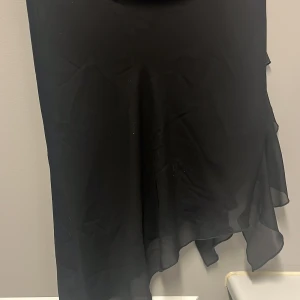 Svart kjol från Miss Selfridge - Säljer en elegant svart kjol från Miss Selfridge i storlek EU 34. Klänningen har en flytande design med asymmetrisk nederkant som ger en fin rörelse. Perfekt för festliga tillfällen eller en utekväll. 🖤
