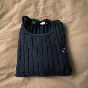 Mörkblå stickad tröja från Gant - Säljer en snygg mörkblå stickad tröja från Gant. Den har ett klassiskt kabelstickat mönster och en liten logga på bröstet. Perfekt för höst och vinter, med långa ärmar och ribbade kanter. Supermysig och stilren! Jag skulle säga att den passar bättre för en 12 åring eller en mindre 13 åring eftersom den är liten i storleken. 💙