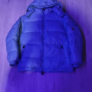 Blå dunjacka från Moncler - Säljer en snygg blå dunjacka från Moncler. Jackan har en pufferstil med dragkedja och långa ärmar. Perfekt för kalla vinterdagar. Den är i mycket bra skick och har en cool etikett med tvättinstruktioner i seriestil. Passar både till vardags och lite finare tillfällen. Använd ca 10 gånger den var för stor så säljer den har triangeln och allt annat men skriv om mer bilder