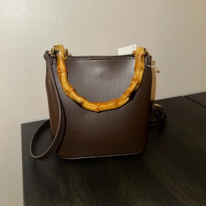 Väska  - Bucket väska med unik detalj!  H&M  Oanvänd, superfint skick  OCH har den perfekta bruna färgen👜🤎