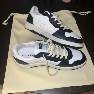 Svartvita sneakers från Axel Arigato - Säljer ett par snygga svartvita sneakers från Axel Arigato i nyskick. De har en stilren design med snörning och är tillverkade i Portugal. Perfekta för både vardag och fest! 🖤🤍 pris kan diskuteras vid snabb affär!