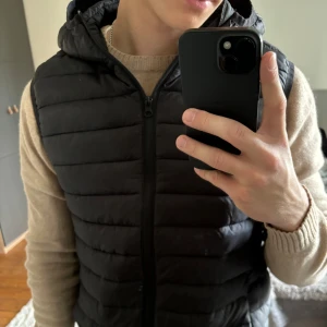 Väst från HM - Säljer en svart väst med luva i bra skick från HM. Inte använd på ca 2 år. Personen på bilden är 180cm lång.