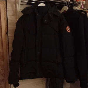 Svart Canada Goose wyndham jacka  - Säljer en svart Canada Goose jacka  i mycket bra skick. Och är perfekt för kalla vinterdagar. Den är långärmad och har en klassisk design med dragkedja och knappar framtill. Supervarm och stilren! Skriv privat för mer info!