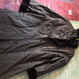 Grön parkajacka med huva - Säljer en grön parkajacka i bra skick. Den har en praktisk huva och knappar framtill. Perfekt för höst och vinter med sin långa ärm och skyddande design. Jackan är både stilren och funktionell.