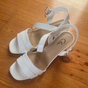 Vita klackskor från Clou - Snygga vita sandaler från Clou i storlek 39. De har en bekväm klack och justerbara remmar med spänne för perfekt passform. Använda en gång☺️✨