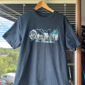 Svart t-shirt med Outer Banks-tryck - Säljer en svart t-shirt med coolt Outer Banks-tryck i vitt och blått. Perfekt för en avslappnad stil. T-shirten är kortärmad och gjord i bomull, vilket gör den skön att bära. Passar bra till både jeans och shorts!