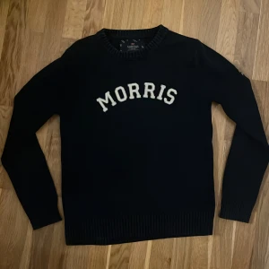 Stickad morris tröja - Snygg svart tröja från Morris med texten 'Morris' i vitt på framsidan. Tröjan har långa ärmar och ribbade kanter vid hals och ärmslut. Perfekt för en stilren look. Aldrig använd!