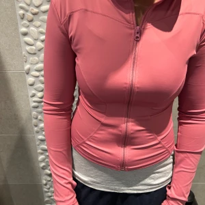 Liknade lululemon tröja - Snygg rosa jacka med dragkedja framtill. Den har en tight passform och långa ärmar, perfekt för träning eller en aktiv vardag.