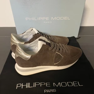 Bruna sneakers från Philippe Model - Snygga bruna sneakers från Philippe Model i mocka med en stilren design. Storlek 39 men passar 40. Skorna har snörning och en vit sula med en diskret rand. Skorna är i väldigt bra skick, andvända ett fåtal gånger. Ny pris: ca: 3000kr Vårt pris:699kr. Skolåda och dust bag följer med.