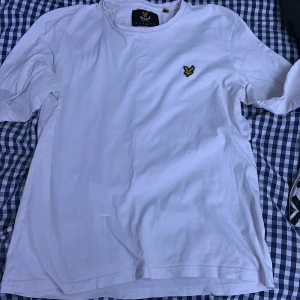 Vit t-shirt med broderad logga - Säljer en klassisk vit t-shirt från Lyle & Scott med en broderad gul logga på bröstet. T-shirten har korta ärmar och är tillverkad i mjukt bomullsmaterial. Perfekt för en avslappnad stil.