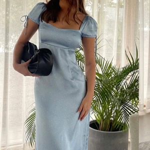 Ljusblå klänning med puffärmar   - Elegant ljusblå klänning med korta puffärmar och en smickrande passform. Klänningen har en subtil prickig design och en vacker fyrkantig urringning. Perfekt för en somrig look. Klänningen säljs inte längre. 