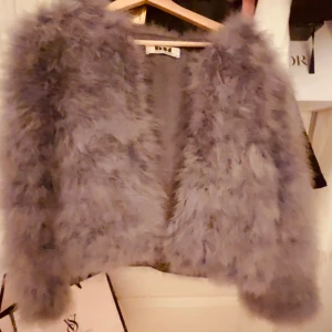 Grå pälsjacka från DM - Säljer en fluffig och trendig grå pälsjacka från Dm. Jackan har en öppen design utan knappar eller dragkedja och är perfekt för att ge en lyxig touch till din outfit. Den är långärmad och gjord i syntetmaterial som ger en mjuk och bekväm känsla. (Andra bilden är lånad) ❣️