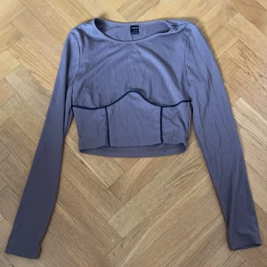 Brun ribbad långärmad topp från Zara - Säljer en bruna ribbade långärmade topp från Zara. Toppen har en unik design med en korsettliknande detalj framtill och är croppad. Perfekt för en trendig look!