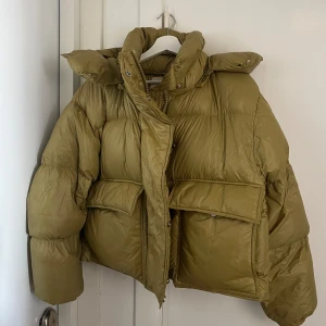 Olivgrön dunjacka från H&M -  pufferjacka från H&M. Jackan är fylld med dun och fjädrar så den är väldigt varm. Köpt förra vintern för 1500kr och använd max 10 gånger. Den har vatten fläckar på ärmarna som jag inte försökt ta bort men borde gå bort direkt i tvätten! Storleken är croppad men lite oversized