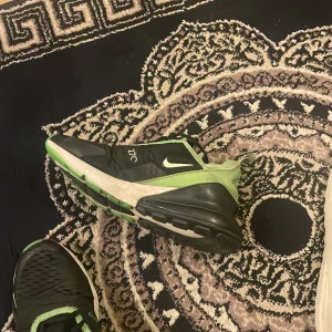 Nike Air Max 270 i svart och grön - Snygga Nike Air Max 270 sneakers i svart och grön med en modern design. Skorna har en synlig Air Max-enhet i hälen för extra komfort och stil. Perfekta för både träning och vardag. Kartongen finns och kan skickas om man vill det.