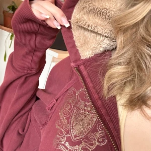 Vinröd hoodie från Billabong - Säljer en mysig vinröd hoodie från Billabong med fluffigt foder i luvan. Den har ett snyggt broderat emblem på ryggen och dragkedja framtill. Perfekt för kyliga dagar!