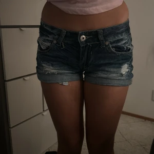 Mörkblå jeansshorts från Chica London - Snygga mörkblå jeansshorts från Chica London med slitna detaljer och upprullade kanter. Perfekta för en avslappnad stil. De har en knapp och dragkedja framtill samt klassiska fem fickor.