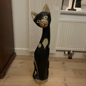 Dekorativ träskulptur av katt - Charmig och stilren träskulptur föreställande en katt. Skulpturen har en svart kropp med vita detaljer och en röd mun. Perfekt som inredningsdetalj för kattälskare.Höjd 82cm. Finns totalt 4 st i olika storlekar