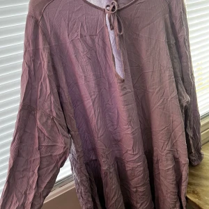 Ljuslila klänning från Divided - Säljer en ljuslila klänning från Divided med knytning vid halsen. Klänningen har en lös passform och långa ärmar, perfekt för en avslappnad stil. Materialet är lätt och luftigt, vilket gör den bekväm att bära.