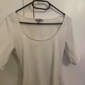 Vit ribbad topp - Säljer en stilren vit ribbad topp med rund halsringning och trekvartsärmar. Perfekt för en enkel och klassisk look. Där är en lite fläck där framme men inget som syns så 